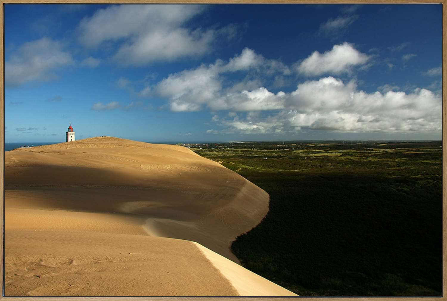 Akustikbild im Eichenrahmen, frontal, Motiv: geschwungene Sanddüne, am Horizont ein kleiner Leuchtturm unter Wolken.
